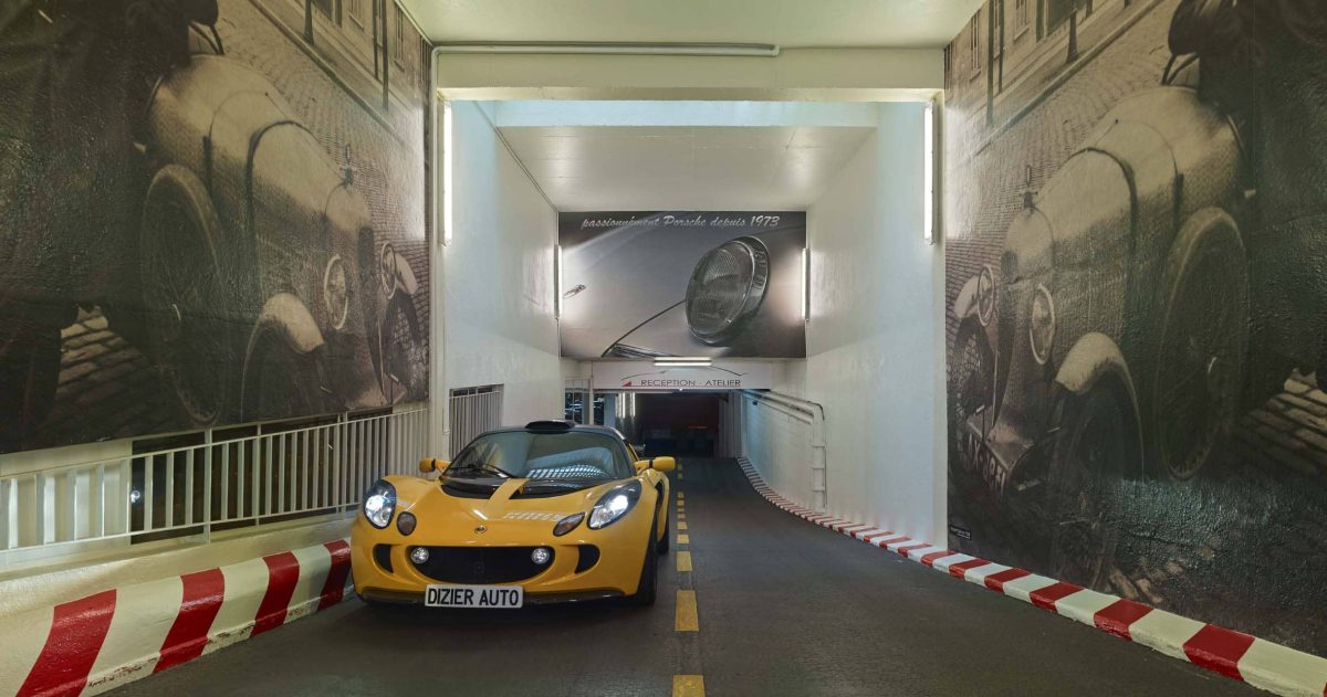 Aménagement d'un accès de garage. Le garage Robert Dizier est reconnu depuis trois générations par les plus grands amateurs de voitures d'exception (Porsche, Lotus, Jaguar, Bentley, ...). Pour référer à la pérennité de cette institution, des impressions numériques HD positionnées sur les murs de la rampe d'accès représentent le fondateur posant devant une Lorraine Dietrich en 1925 et devant une Amilcar en 1938.