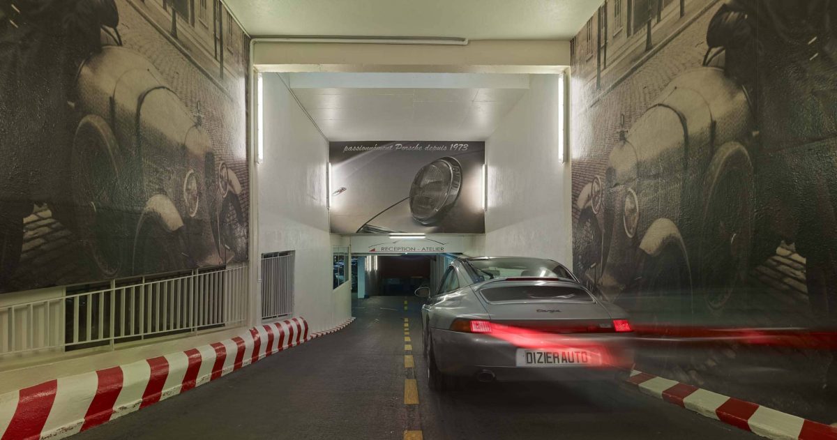 Aménagement d'un accès de garage. Le garage Robert Dizier est reconnu depuis trois générations par les plus grands amateurs de voitures d'exception (Porsche, Lotus, Jaguar, Bentley, ...). Pour référer à la pérennité de cette institution, des impressions numériques HD positionnées sur les murs de la rampe d'accès représentent le fondateur posant devant une Lorraine Dietrich en 1925 et devant une Amilcar en 1938.